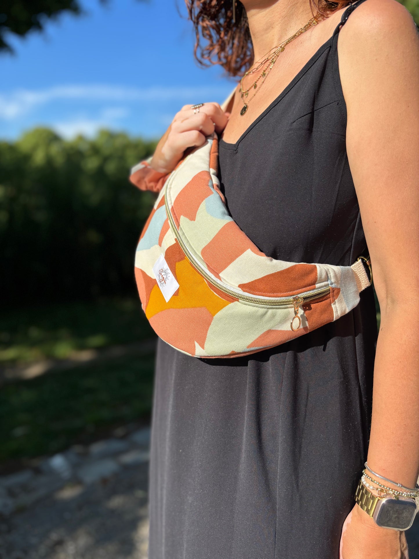 Banane multi color portée en bandoulière par une femme dans un parc ensoleillé, symbole de liberté et de style au quotidien. Ce modèle allie audace et douceur, parfait pour garder les mains libres avec élégance. Confectionnée à la main avec un tissu jacquard de qualité, elle ne se déforme pas et conserve sa tenue. Idéale pour accompagner les journées actives avec une touche de féminité bohème.