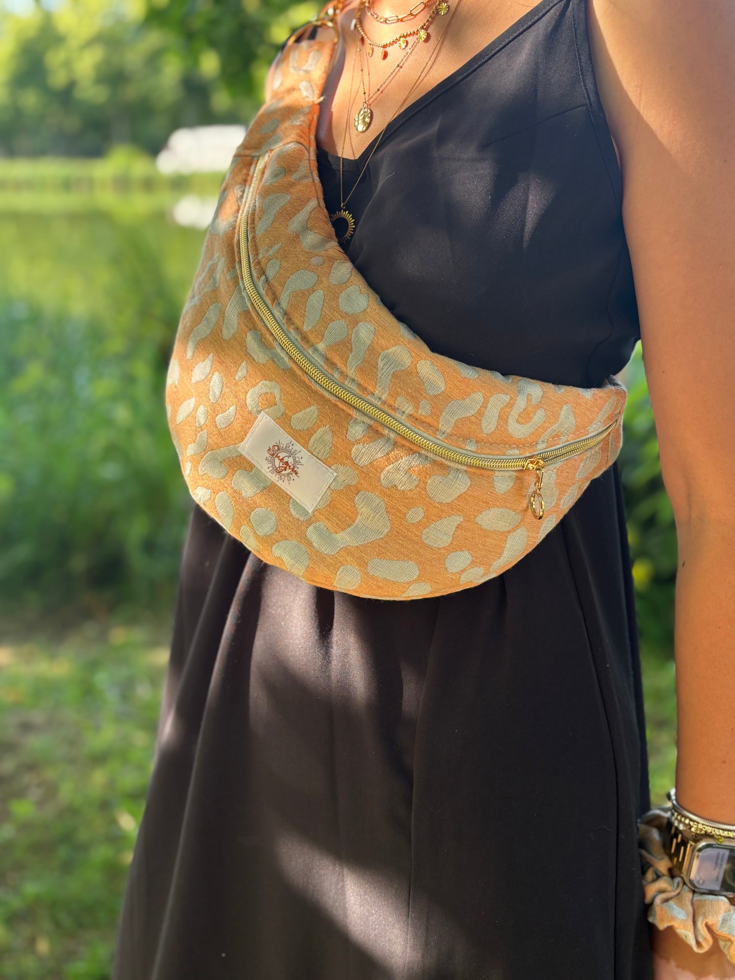 Banane léopard orange portée en bandoulière par une femme dans un parc ensoleillé, symbole de liberté et de style au quotidien. Ce modèle allie audace et douceur, parfait pour garder les mains libres avec élégance. Confectionnée à la main avec un tissu jacquard de qualité, elle ne se déforme pas et conserve sa tenue. Idéale pour accompagner les journées actives avec une touche de féminité bohème.