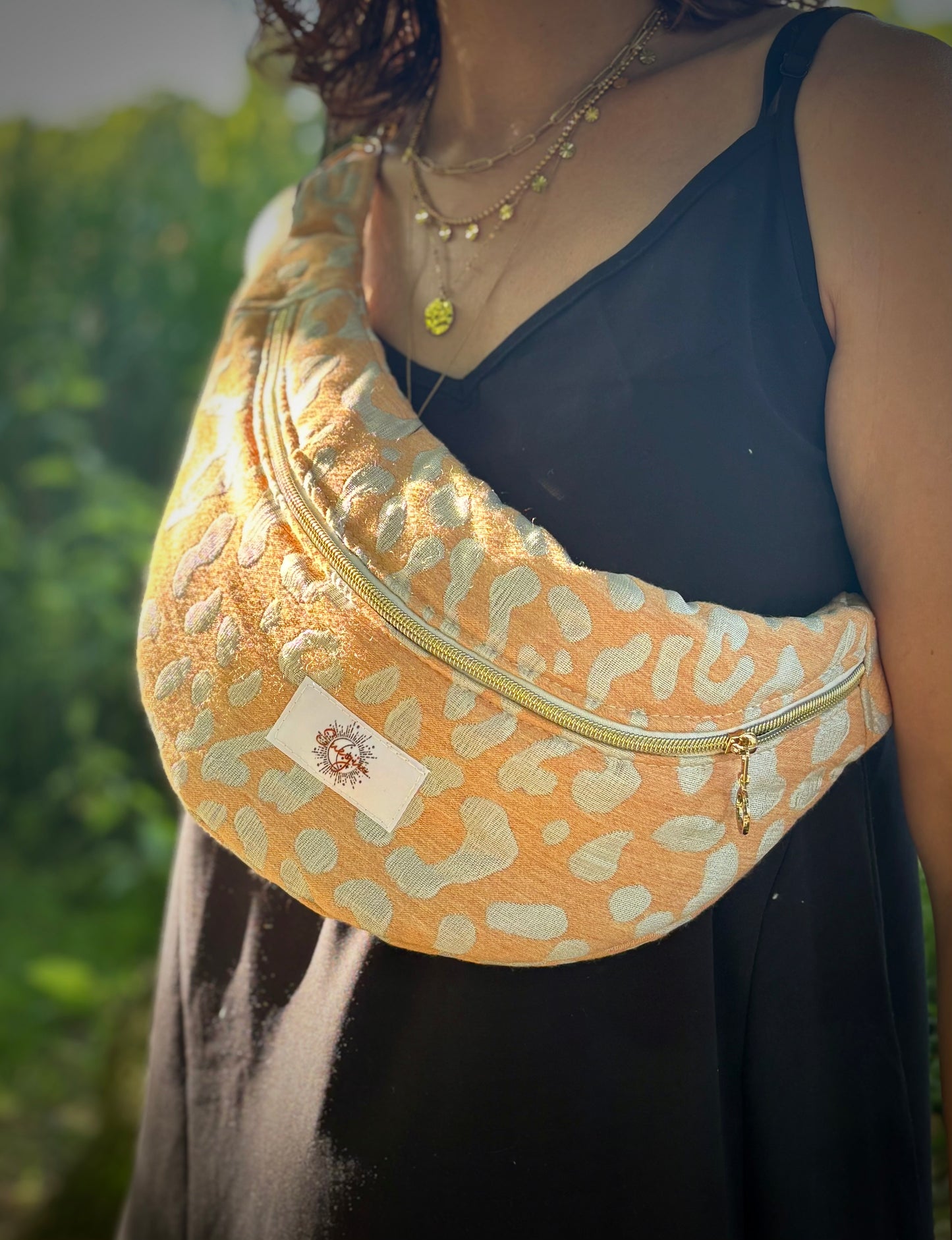 Banane léopard orange portée en bandoulière par une femme dans un parc ensoleillé, symbole de liberté et de style au quotidien. Ce modèle allie audace et douceur, parfait pour garder les mains libres avec élégance. Confectionnée à la main avec un tissu jacquard de qualité, elle ne se déforme pas et conserve sa tenue. Idéale pour accompagner les journées actives avec une touche de féminité bohème.