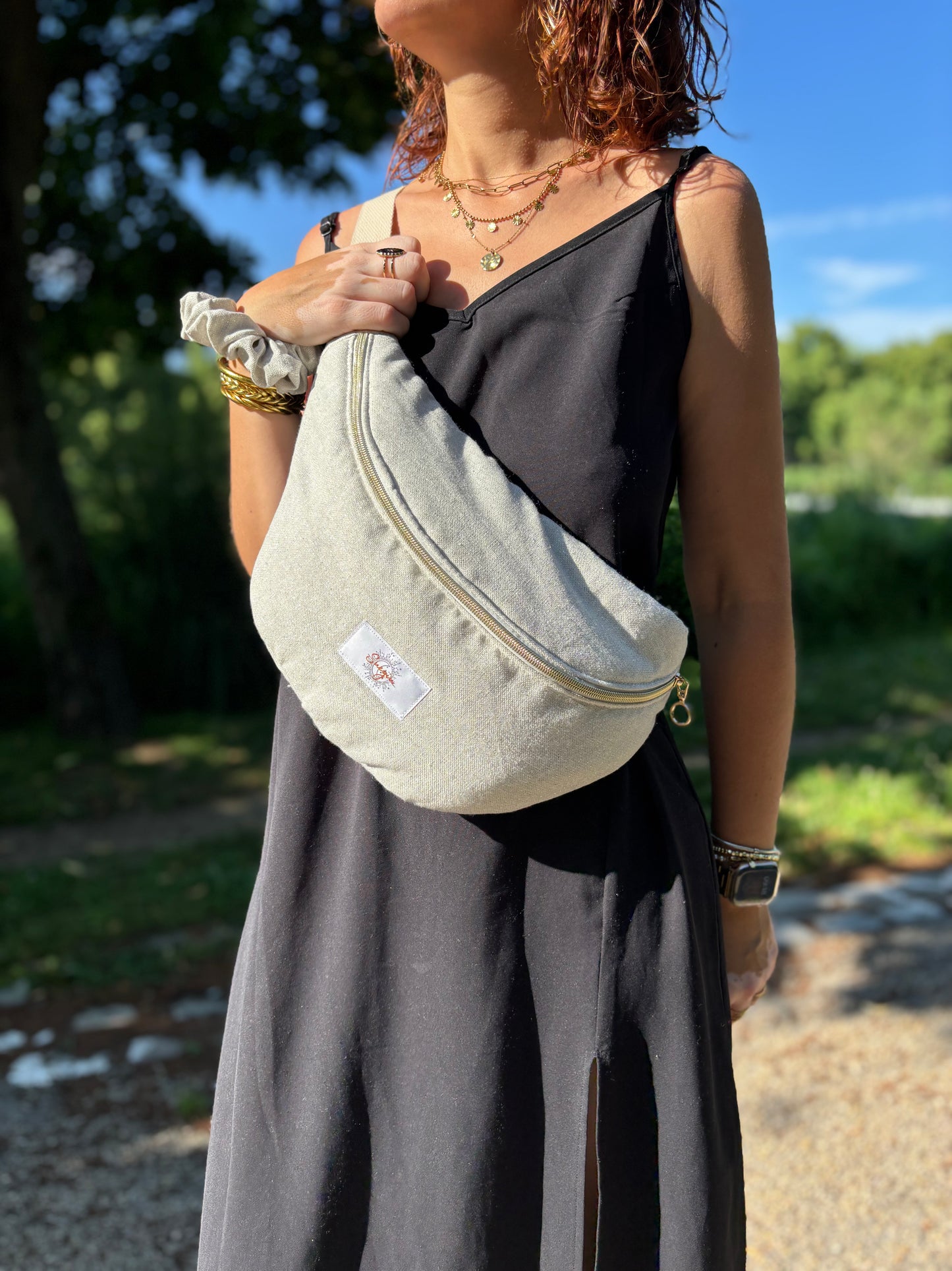 Banane beige pailleté portée en bandoulière par une femme dans un parc ensoleillé, symbole de liberté et de style au quotidien. Ce modèle allie audace et douceur, parfait pour garder les mains libres avec élégance. Confectionnée à la main avec un tissu jacquard de qualité, elle ne se déforme pas et conserve sa tenue. Idéale pour accompagner les journées actives avec une touche de féminité bohème.