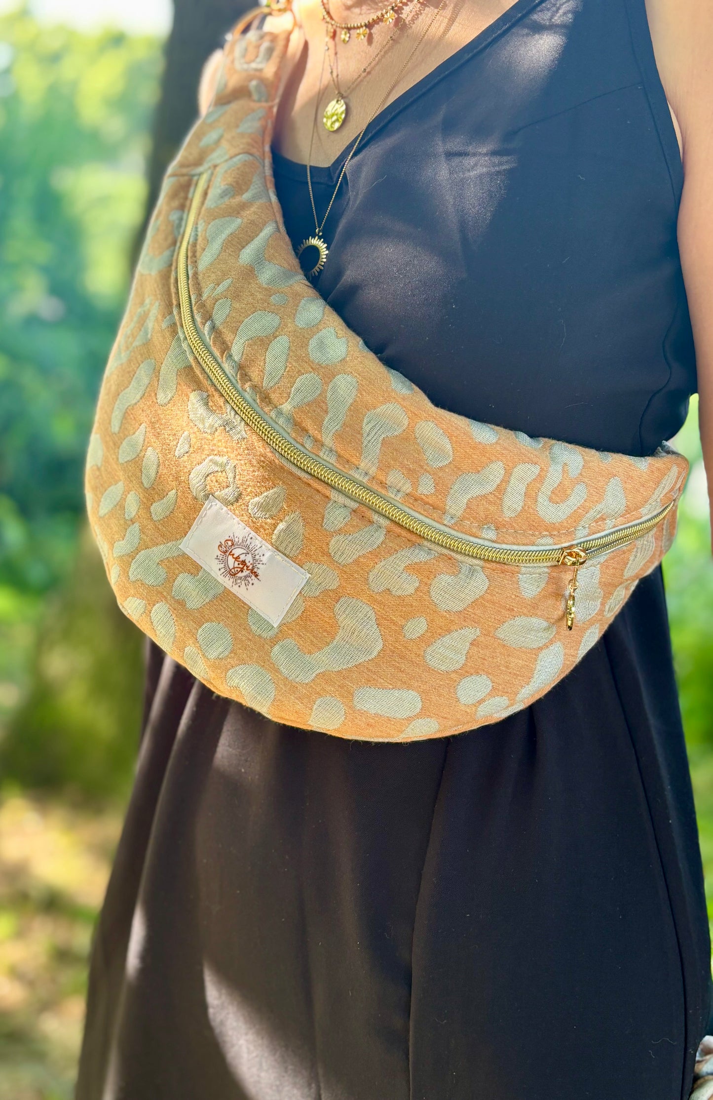 Banane léopard orange portée en bandoulière par une femme dans un parc ensoleillé, symbole de liberté et de style au quotidien. Ce modèle allie audace et douceur, parfait pour garder les mains libres avec élégance. Confectionnée à la main avec un tissu jacquard de qualité, elle ne se déforme pas et conserve sa tenue. Idéale pour accompagner les journées actives avec une touche de féminité bohème.