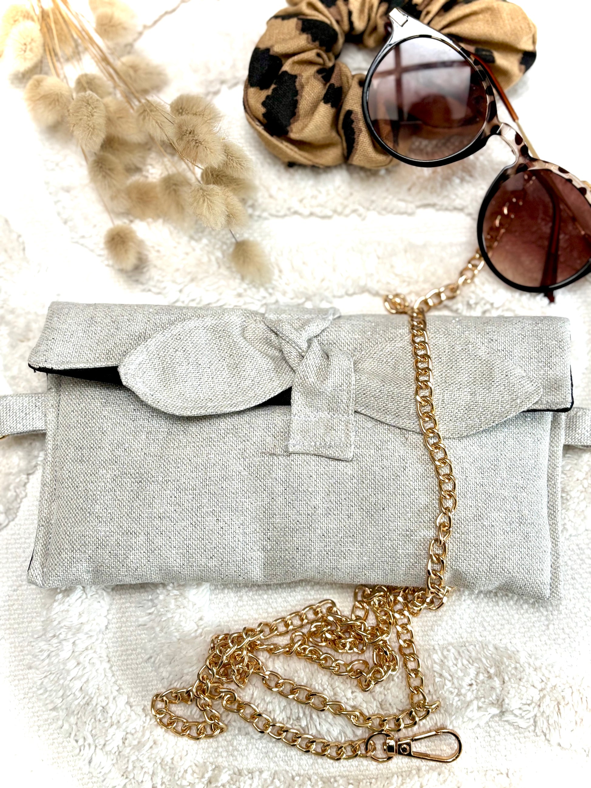 Pochette  Alma beige pailleté  posée sur une table, associant élégance discrète et praticité. Pensée comme une caméléon du quotidien, elle accompagne aussi bien les journées chargées que les soirées improvisées. Son tissu structuré haut de gamme lui permet de garder sa forme. Entièrement fabriquée à la main, elle peut aussi se transformer en petit sac raffiné avec sa sangle amovible.