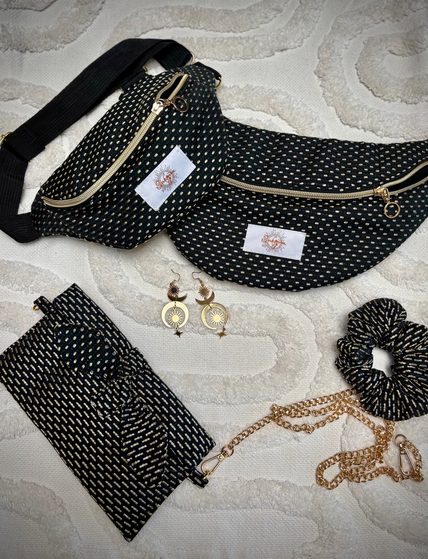 Banane noir et or, symbole de liberté et de style au quotidien. Ce modèle allie audace et douceur, parfait pour garder les mains libres avec élégance. Confectionnée à la main avec un tissu jacquard de qualité, elle ne se déforme pas et conserve sa tenue. Idéale pour accompagner les journées actives avec une touche de féminité bohème.