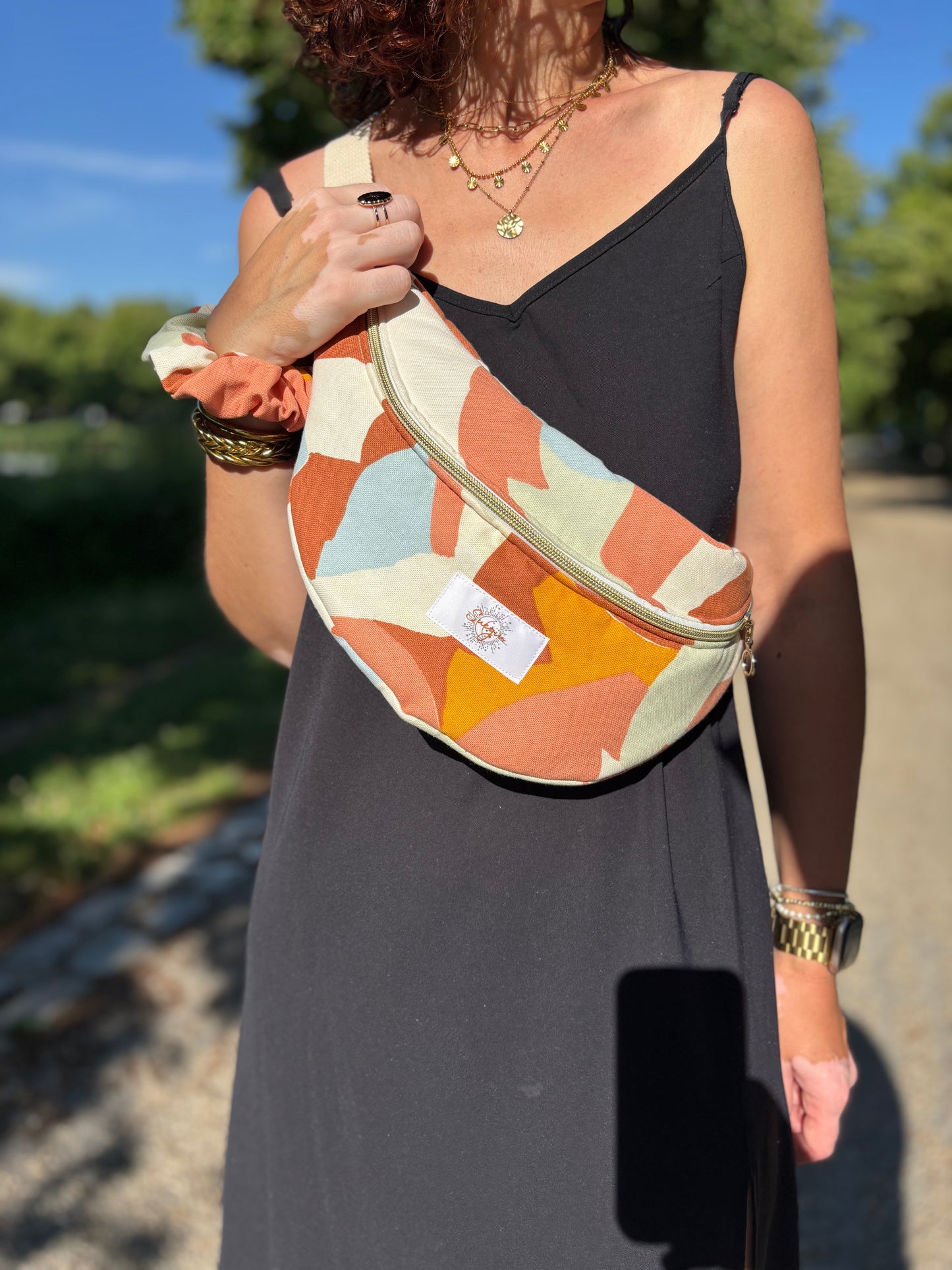 Banane multi color portée en bandoulière par une femme dans un parc ensoleillé, symbole de liberté et de style au quotidien. Ce modèle allie audace et douceur, parfait pour garder les mains libres avec élégance. Confectionnée à la main avec un tissu jacquard de qualité, elle ne se déforme pas et conserve sa tenue. Idéale pour accompagner les journées actives avec une touche de féminité bohème.