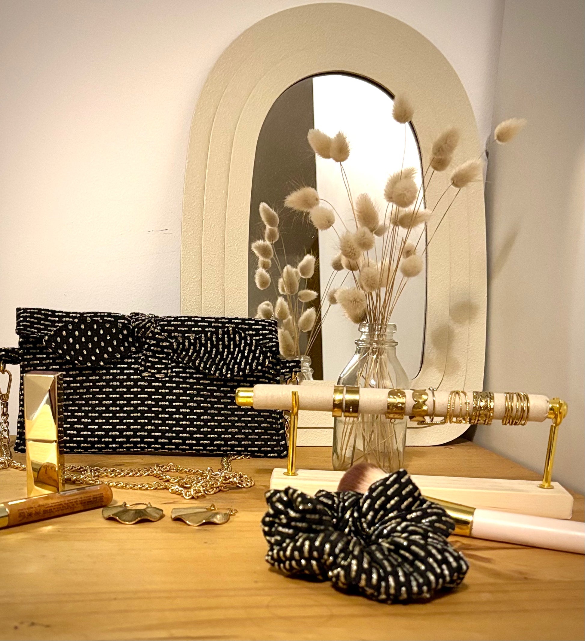 Trousse noire Alma de SueGiu posée à plat, avec sa forme rectangulaire et ses détails sobres et élégants. Tissu texturé noir profond, fermeture éclair dorée, sur coiffeuse élegance et chic