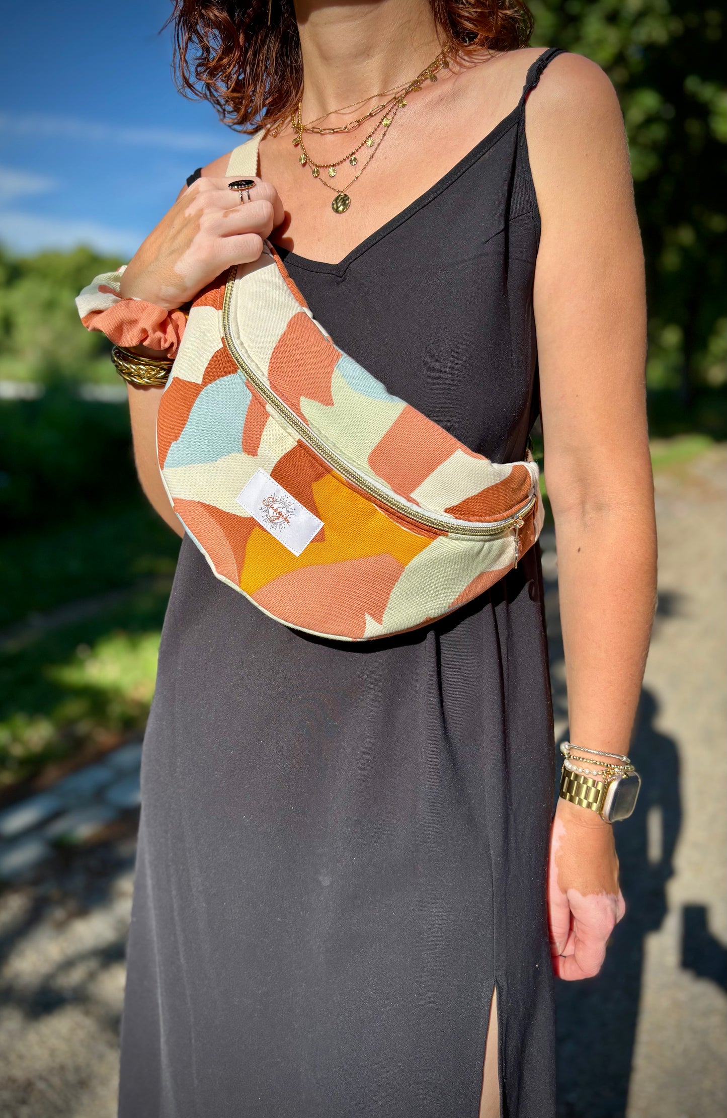 Banane multi color portée en bandoulière par une femme dans un parc ensoleillé, symbole de liberté et de style au quotidien. Ce modèle allie audace et douceur, parfait pour garder les mains libres avec élégance. Confectionnée à la main avec un tissu jacquard de qualité, elle ne se déforme pas et conserve sa tenue. Idéale pour accompagner les journées actives avec une touche de féminité bohème.