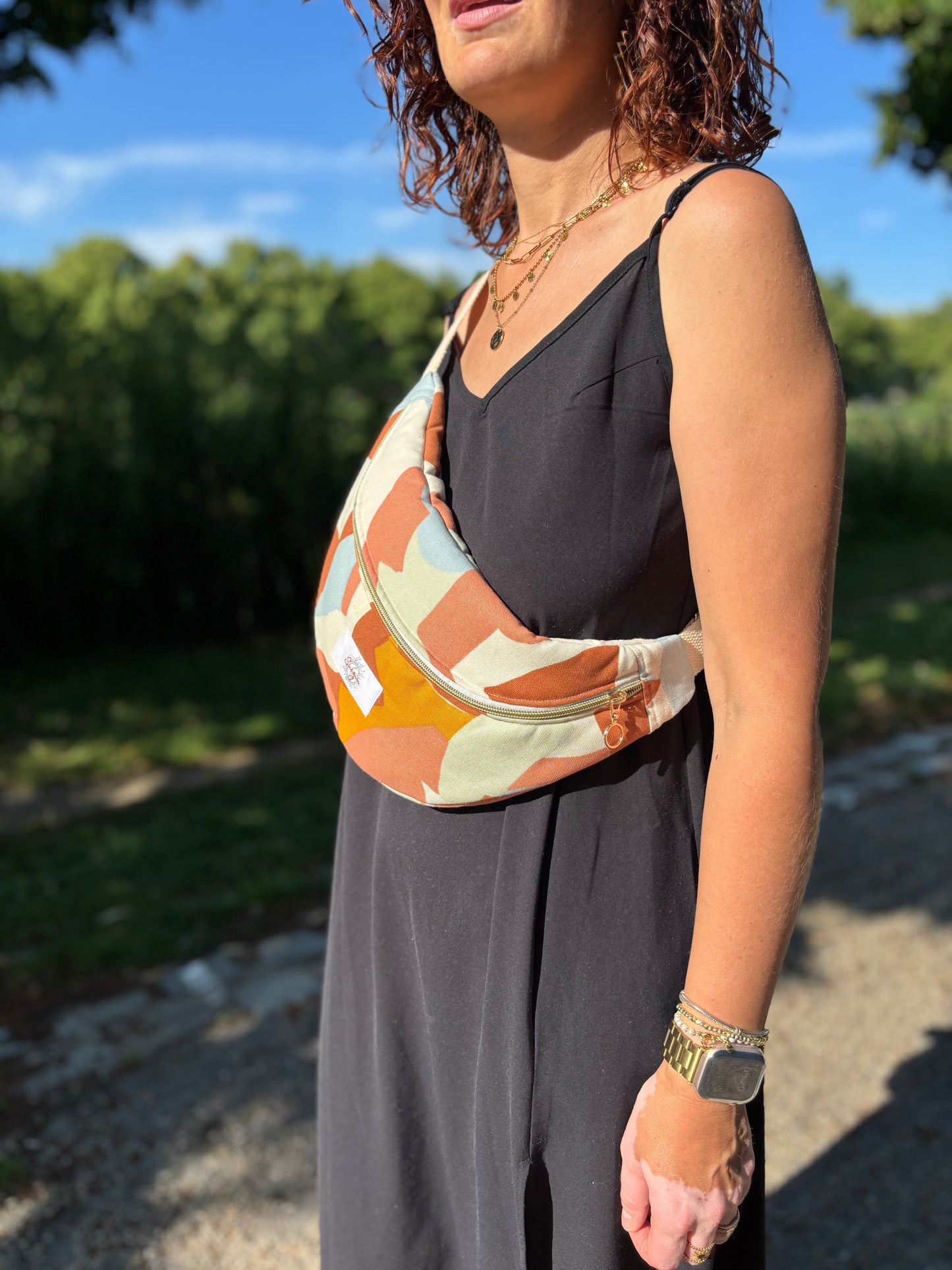 Banane multi color portée en bandoulière par une femme dans un parc ensoleillé, symbole de liberté et de style au quotidien. Ce modèle allie audace et douceur, parfait pour garder les mains libres avec élégance. Confectionnée à la main avec un tissu jacquard de qualité, elle ne se déforme pas et conserve sa tenue. Idéale pour accompagner les journées actives avec une touche de féminité bohème.