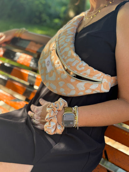 Banane  léopard orange portée en bandoulière par une femme dans un parc ensoleillé, symbole de liberté et de style au quotidien. Ce modèle allie audace et douceur, parfait pour garder les mains libres avec élégance. Confectionnée à la main avec un tissu jacquard de qualité, elle ne se déforme pas et conserve sa tenue. Idéale pour accompagner les journées actives avec une touche de féminité bohème.