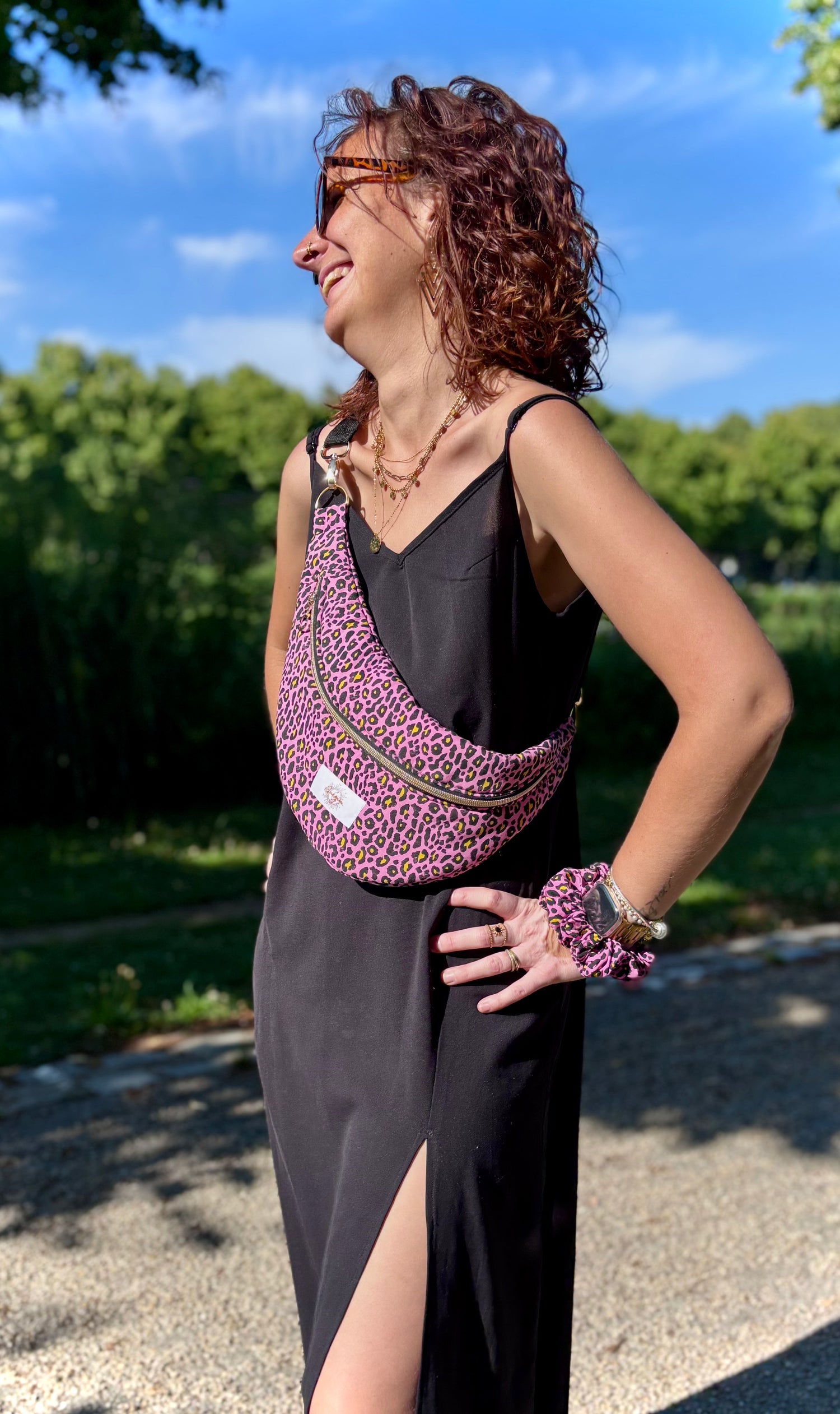 Banane rose léopard portée en bandoulière par une femme dans un parc ensoleillé, symbole de liberté et de style au quotidien. Ce modèle allie audace et douceur, parfait pour garder les mains libres avec élégance. Confectionnée à la main avec un tissu jacquard de qualité, elle ne se déforme pas et conserve sa tenue. Idéale pour accompagner les journées actives avec une touche de féminité bohème.